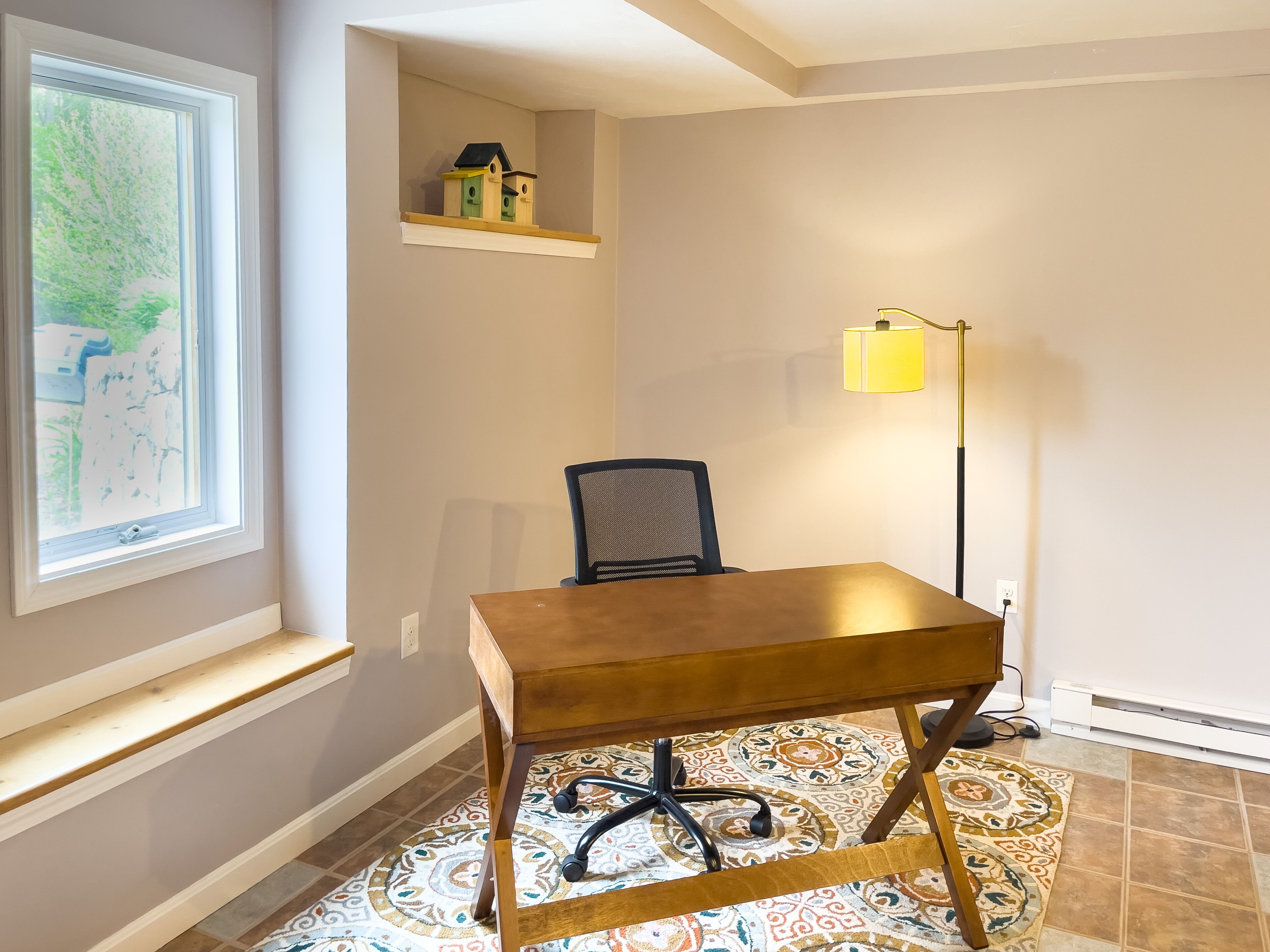 A room with a wooden desk, a chair, a lamp, a map on the wall, and a small shelf with a model house.
