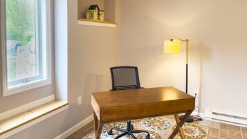 A room with a wooden desk, a chair, a lamp, a map on the wall, and a small shelf with a model house.