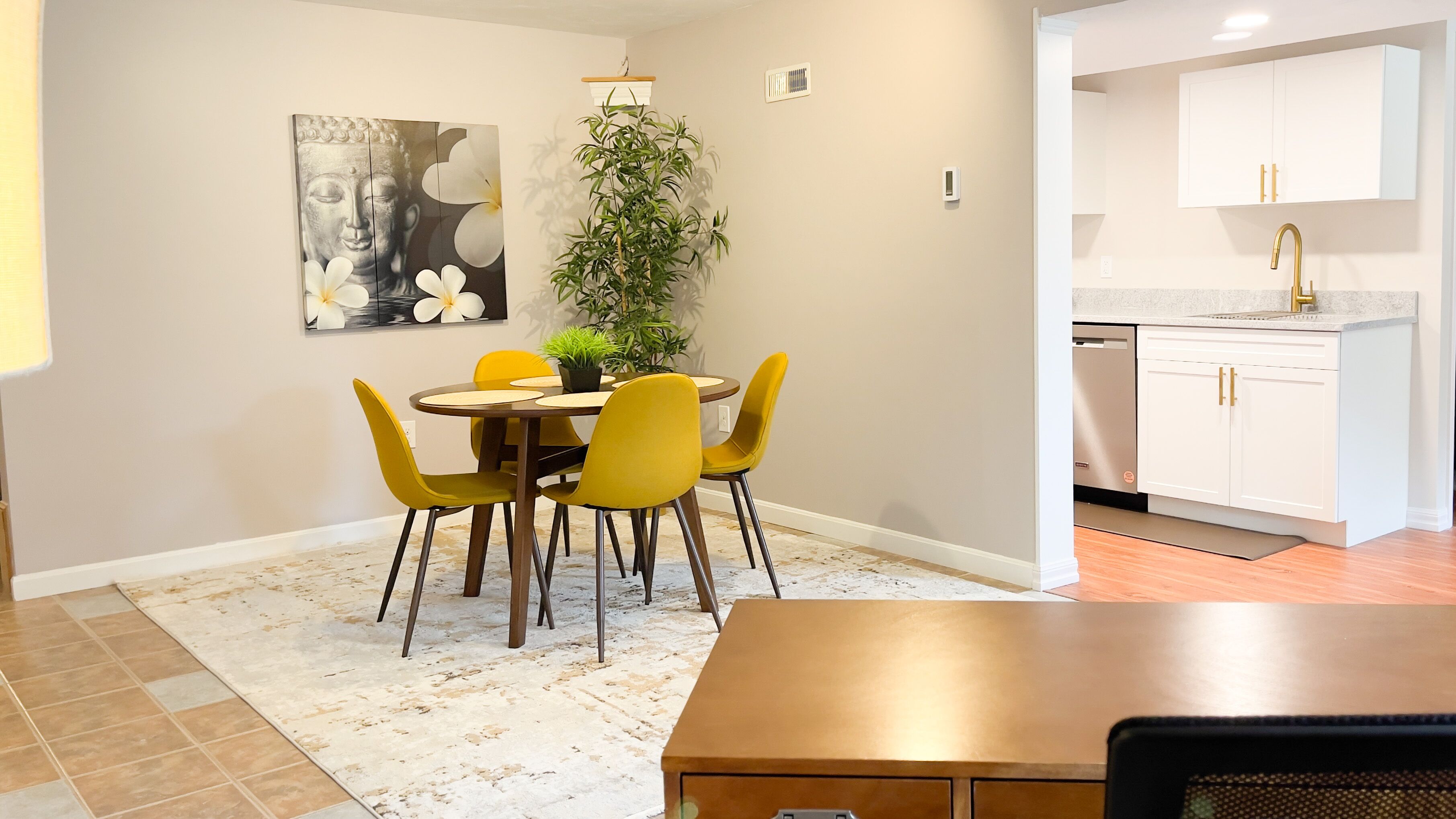 A dining area with a round table, yellow chairs, a potted plant, and a Buddha painting on the wall.