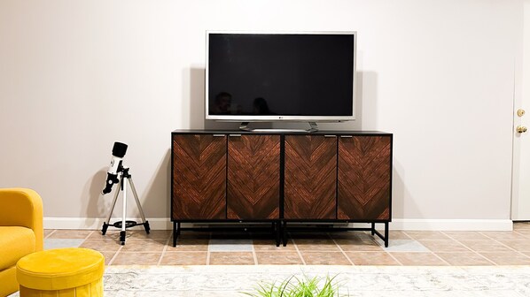 Un salon moderne avec un téléviseur à écran plat posé sur un meuble en bois, un fauteuil jaune et un télescope sur un trépied.
