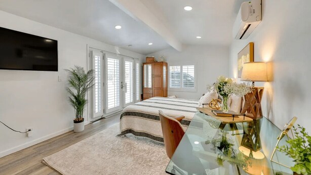 A modern bedroom with a large bed, a glass desk, a TV mounted on the wall, and a potted plant. - Midterm Escape  Mountain Views & Desert Breezes (Palm Springs)