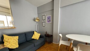 A living room with a grey sofa, two yellow pillows, a small table, and a white chair. - Cosy Studio in Recoleta, Buenos Aires. Walking distance from mayor attractions (CABA)