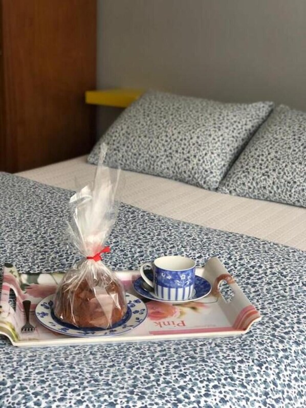 Un lit avec une couvre-lit à motifs, un plateau avec une tasse de thé et un objet emballé, et un magazine sur le lit.