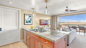 A kitchen with granite countertops, wooden cabinets, a built-in sink, and a dining area with a view. - Maui Resort Rentals: Honua Kai - 3 Total Bedrooms,  8th Floor "Penthouse" Ocean AND West Maui Mountain Views, Deluxe Corner Floor Plan! (Lahaina)