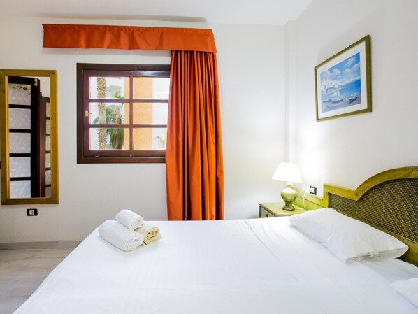 A hotel room with a bed, a window with curtains, a bedside lamp, and a painting on the wall.