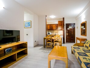 Un salon avec un téléviseur, des meubles en bois, un canapé et une cuisine à l’arrière-plan.