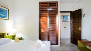 A hotel room with a bed, a wooden wardrobe, a nightstand with a lamp, and a painting on the wall. - 104 Andorra close to the beach (Playa de las Américas)