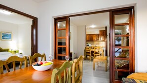 A dining area with a wooden table, chairs, and a bowl of fruit. There is a kitchen visible through an open doorway. - 104 Andorra close to the beach (Playa de las Américas)