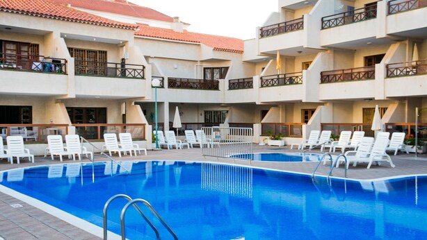 A swimming pool with white lounge chairs and a tiled deck. - 104 Andorra close to the beach (Playa de las Américas)