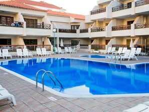 A swimming pool with white lounge chairs and a tiled deck.