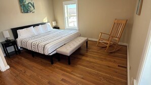 Une chambre à coucher comprenant un lit, un banc, un fauteuil à bascule, une table de chevet et un ventilateur de plafond.