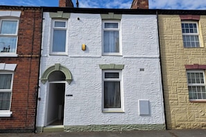 A two-story building with a white textured facade, a green door, and a small window with a yellow light fixture. - Seaside cosy Cottage Escape in Bridlington (Bridlington)