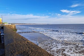 A coastal view with a stone sea wall, waves, and a distant shoreline.