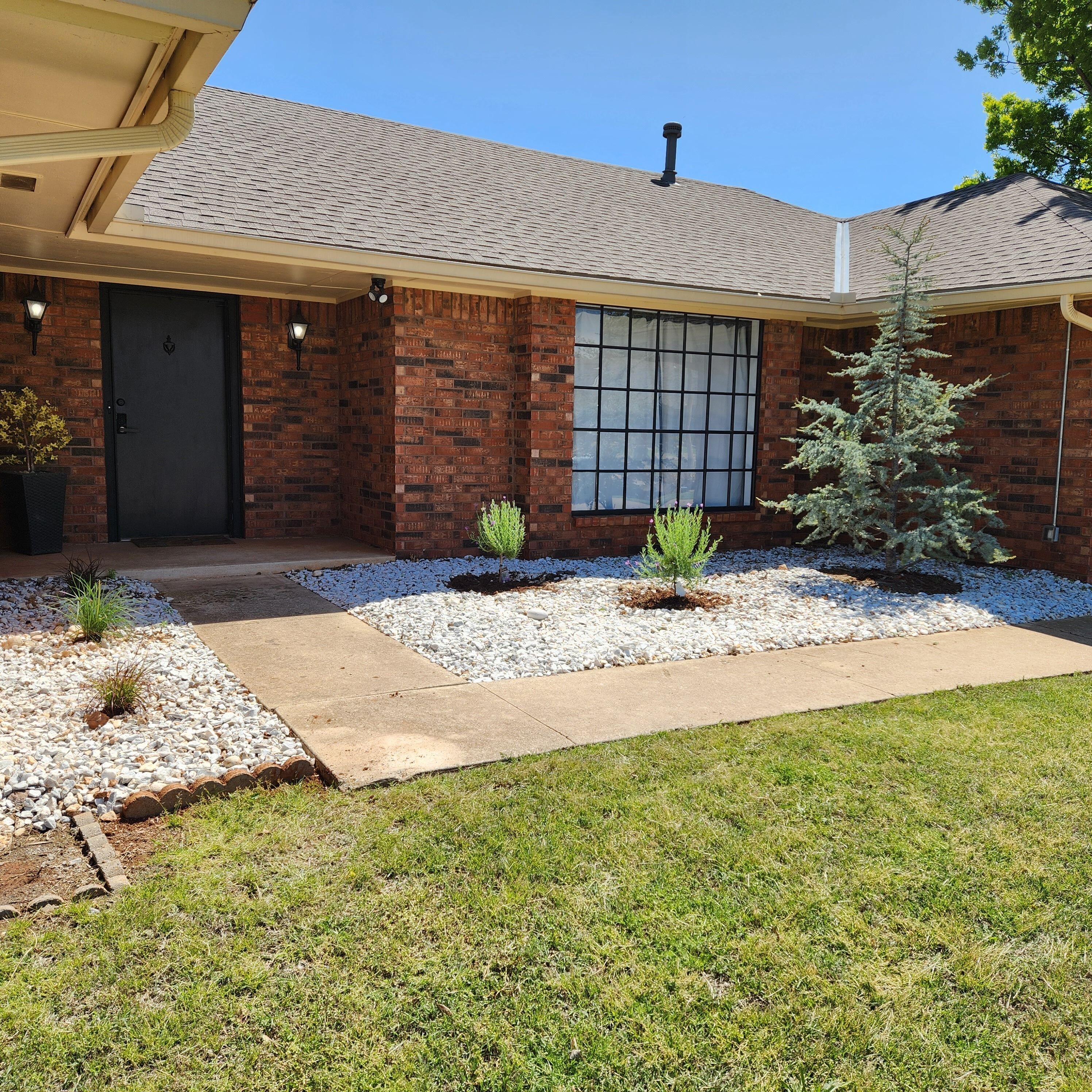 A house with a brick exterior, a front door, a window, and a small tree in the front yard.