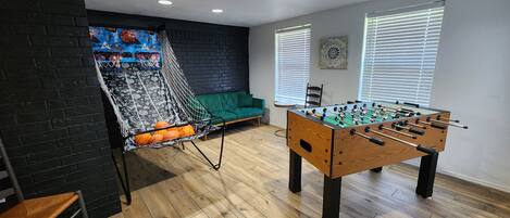A room with a foosball table, a hammock with basketballs, a green couch, and a brick wall.