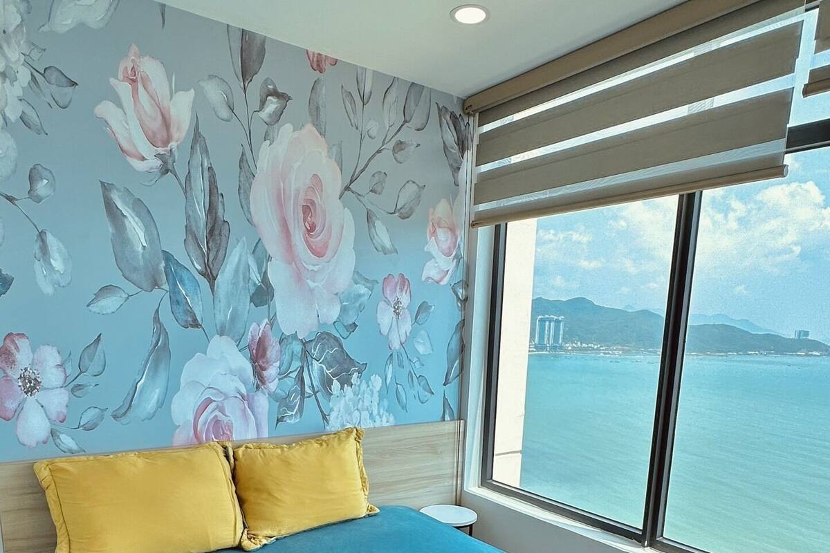 A bedroom with a large bed, a view of the sea, and a floral wall mural.