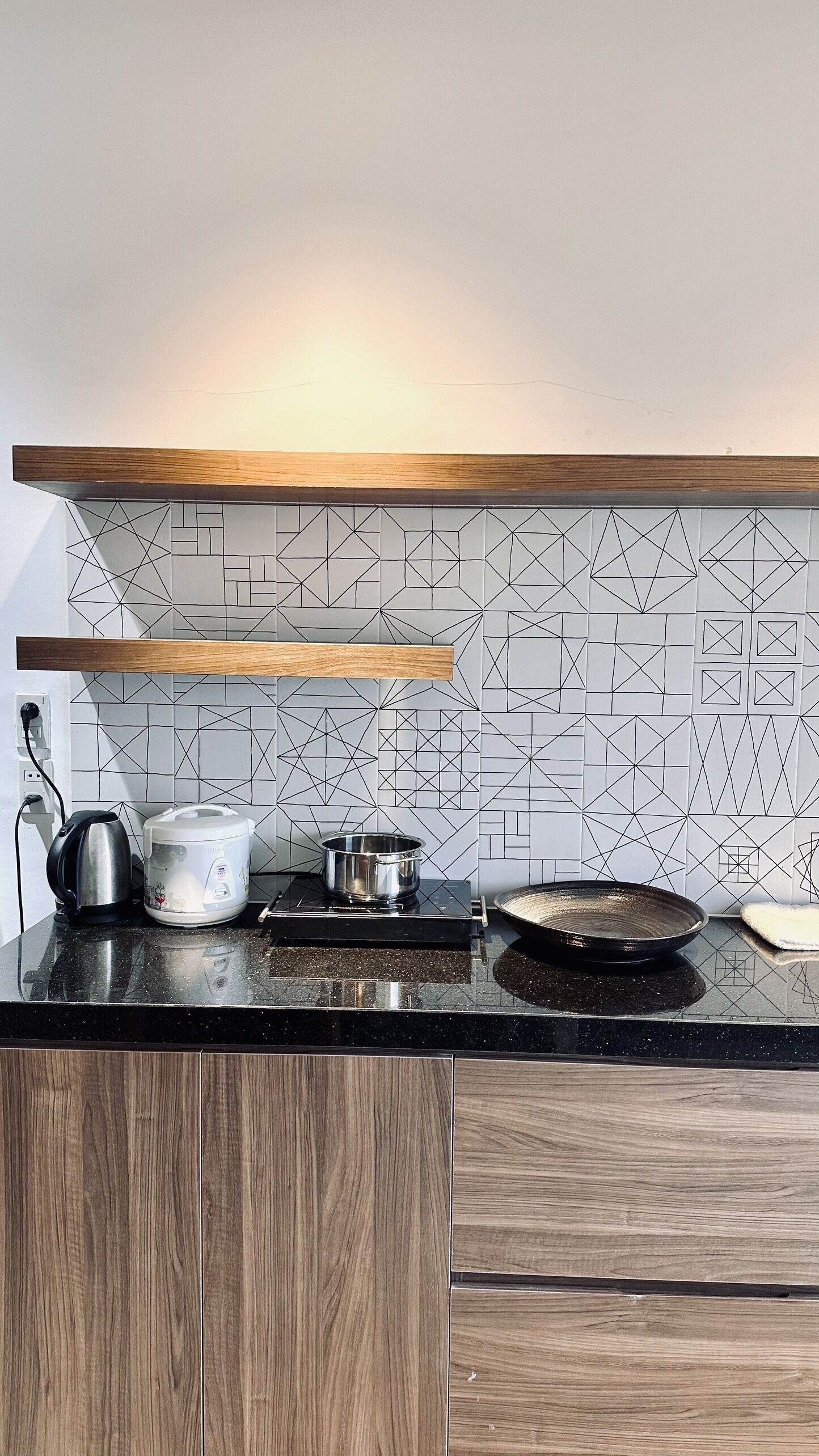 Eine Küche mit schwarzem Arbeitsplatz, Holzschränken, einer geometrischen Spritzschutzwand und einem Holzregal darüber.