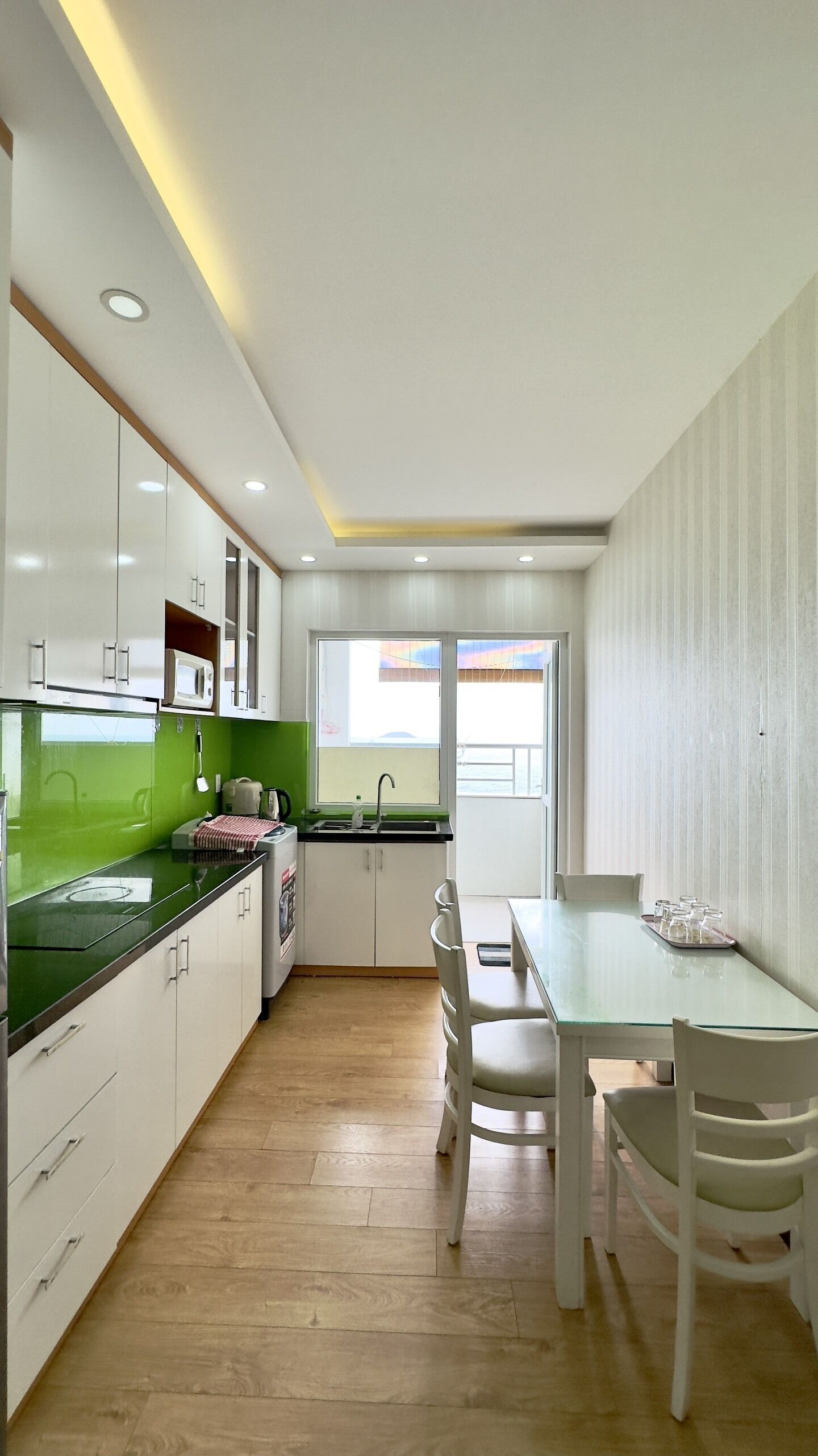 A modern kitchen with white cabinets, a green countertop, and a dining area with a glass table and chairs.