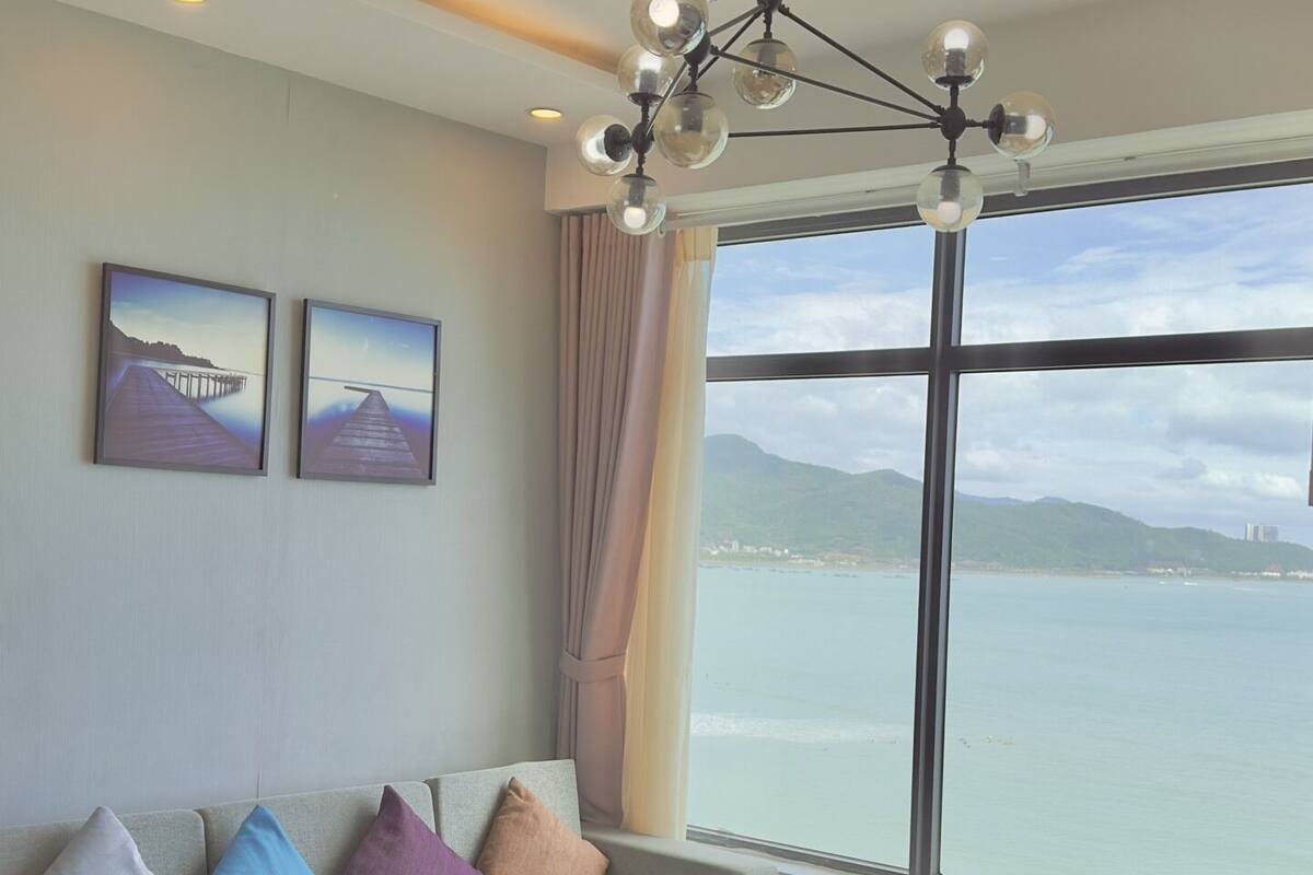 A modern living room with a grey sofa, a white coffee table, and a view of the sea through large windows.