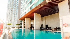 A swimming pool with lounge chairs and umbrellas, surrounded by a modern building with large windows and a wooden ceiling.