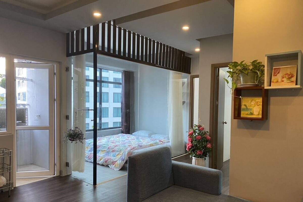A modern hotel room with a large bed, a seating area, a balcony, and a view of the city.