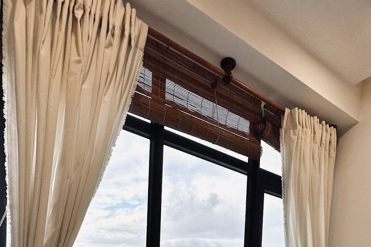 A hotel room with a bed, a window with curtains, and a view of a cityscape and mountains.