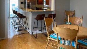 Een moderne keuken met een centraal eiland, barstoelen en een eettafel met stoelen.