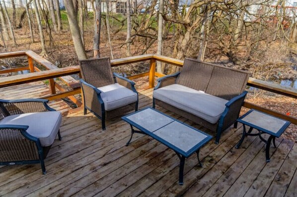 Relax on the deck with a sofa, armchairs, and a small table, surrounded by a serene wooded view.