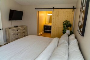 Relax in this serene bedroom with a large bed and a mounted TV, featuring a convenient bathroom access and a touch of greenery.