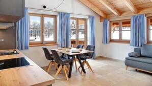 Una cocina moderna con comedor, vigas de madera en el techo y ventanas amplias con cortinas.
