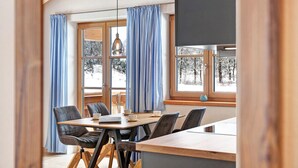 Un comedor con mesa de madera, sillas y vistas a árboles nevados a través de ventanas grandes.