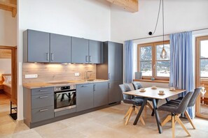 Een moderne keuken met grijze kastjes, een houten aanrechtblad en een eethoek met tafel en stoelen.