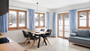 Ein moderner Essbereich mit Holztisch und -stühlen, einer Couch und großen Fenstern mit Vorhängen.