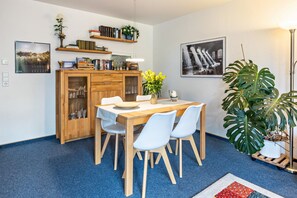 Un coin repas comprenant une table en bois, des chaises, un meuble avec des portes en verre, une plante en pot et des œuvres d’art murales.