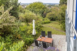 Une terrasse avec une table et des chaises, entourée d’une végétation luxuriante et bordée d’un chemin pavé.