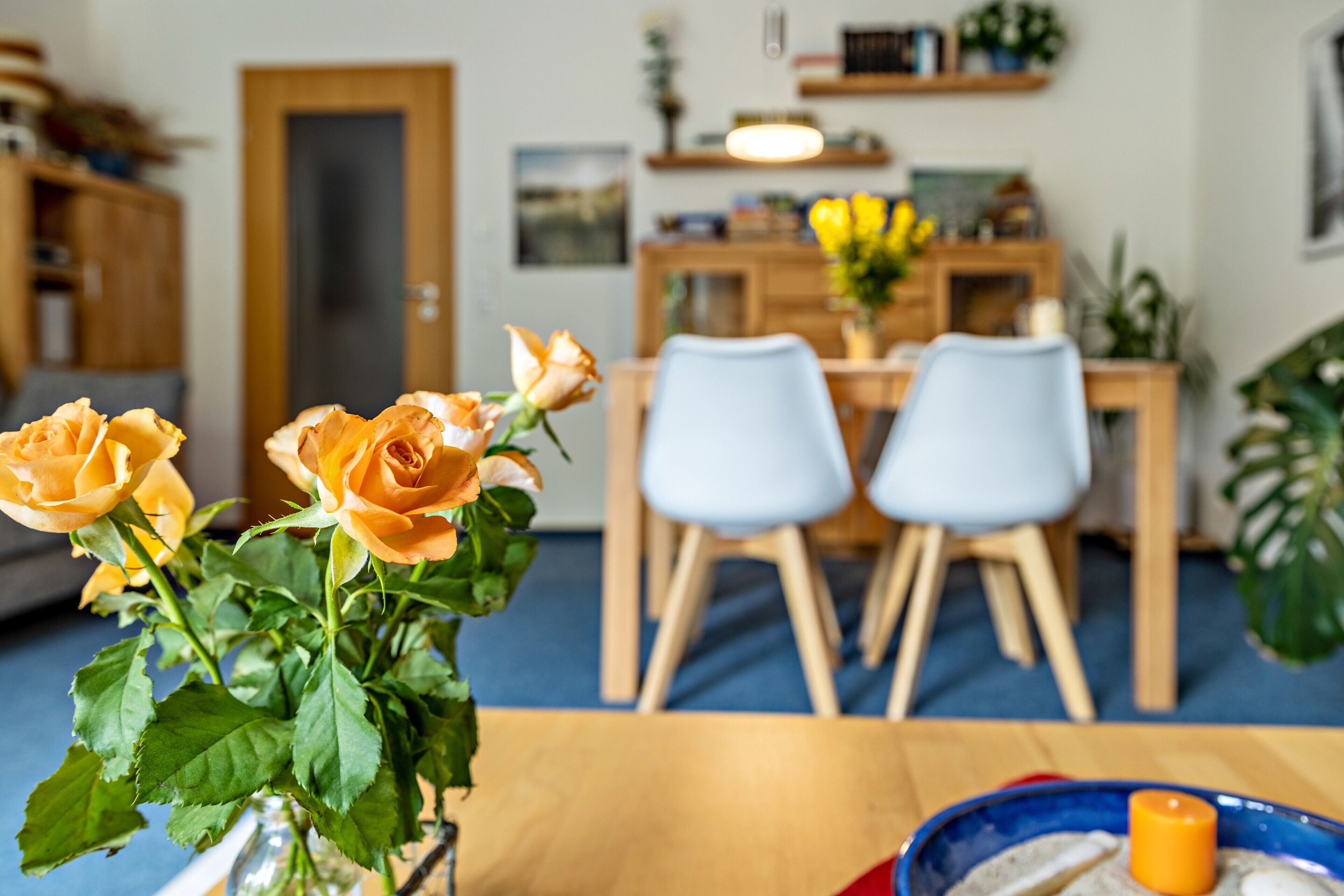 Een eetruimte met een houten tafel, twee stoelen, een vaas met bloemen en een deur op de achtergrond.