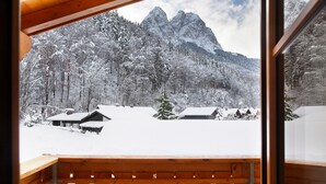 Un balcon en bois offrant une vue sur des arbres et des montagnes enneigés.