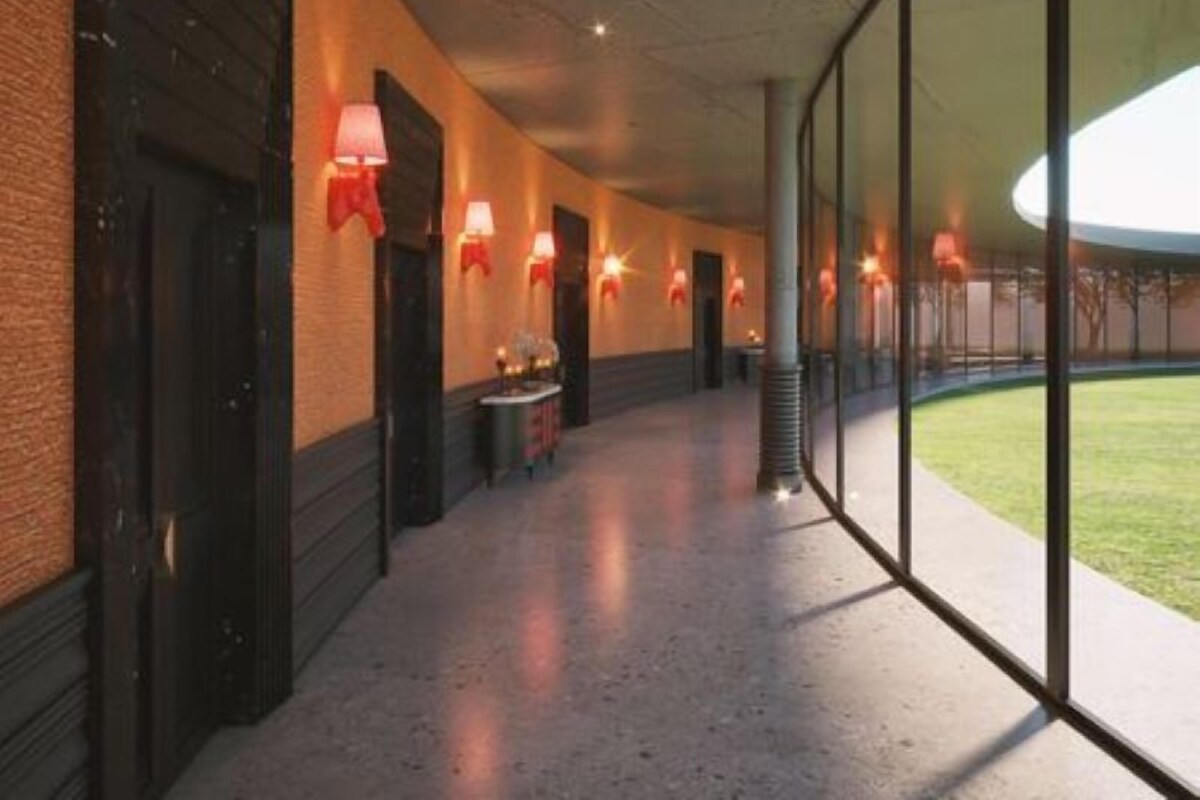 Un couloir avec une paroi en verre d’un côté, un mur de briques de l’autre, et une rangée de lampes rouges le long du plafond.