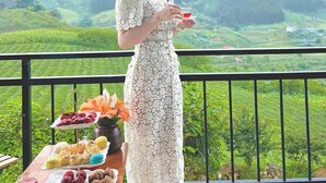 A woman in a white lace dress standing on a balcony with a table of snacks and a glass of red drink. - Vigolando Van Ho Resort (Van Ho)
