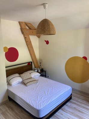 A bedroom with a bed, wooden headboard, bedside table, and a hanging light fixture.