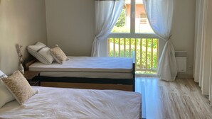 A bedroom with two beds, a window with curtains, a red hanging light, and a wooden floor. - Villa Morgon (SAVINES LE LAC)