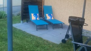 A covered outdoor seating area with two blue lounge chairs and a barbecue grill. - Villa Morgon (SAVINES LE LAC)