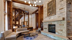 A spacious living area with a stone fireplace, a sofa set, a coffee table, and a staircase leading to an upper level. - Abode at First Dawn, ski-in/ski-out, hot tub, sauna, resort access (Park City)