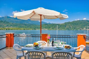 A table set with plates, glasses, and a bottle, overlooking a lake with mountains in the background.
