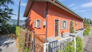A two-story building with a red facade, white shutters, and a balcony with potted plants. - Red House: Beachfront Terrace & Private Beach, Baveno, Italy (Baveno)