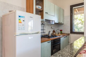 A kitchen with a white refrigerator, wooden cabinets, a stove, and a window. - Trilo Debora 2Km From The Beach, Porto San Paolo, Italy (Porto San Paolo)