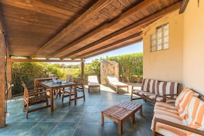 An outdoor patio with wooden furniture, a stone wall, and a view of greenery.