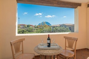 Un balcon avec une table, deux chaises, une bouteille de vin et deux verres.