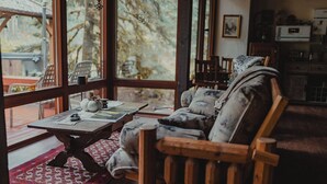 A cozy room with a wooden sofa, a table with a teapot, and a view of the outdoors through large windows.