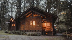 A rustic cabin with a wooden exterior, a porch, and a gravel driveway.